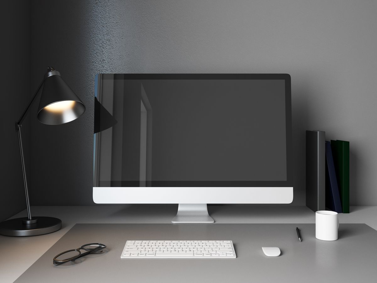 A clean designer desk with a monitor and lamp